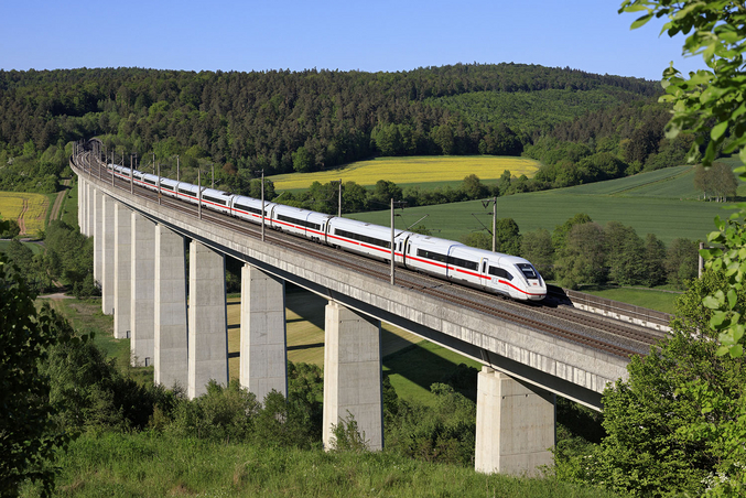 Ein weißer ICE fährt über eine Brücke vor grüner Landschaft