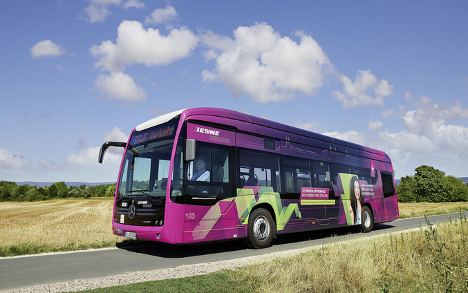 Ein lila ESWE E-Bus auf einer Feldstraße vor blauem Himmel.