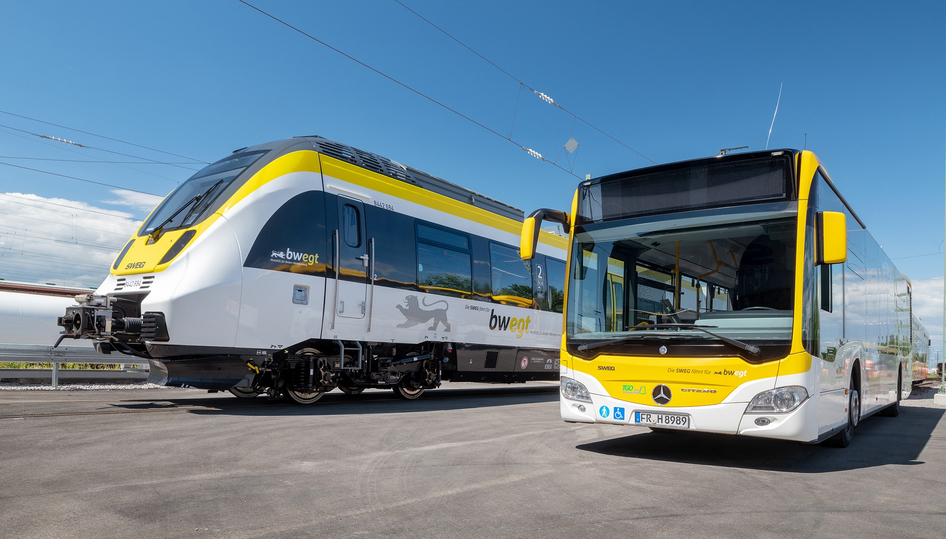 Ein leerer gelb-weißer Bus sowie ein gelb-weißer Zug der SWEG stehen nebeneinander auf einem Betriebshof.