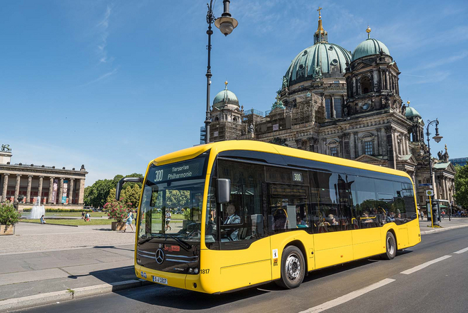 Ein gelber Mercedes Benz eCitaro unter blauem Himmel vor dem Berliner Dom.