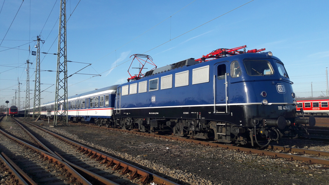 Ein blauer Zug der TRI fährt von links nach rechts über braune Schienen.